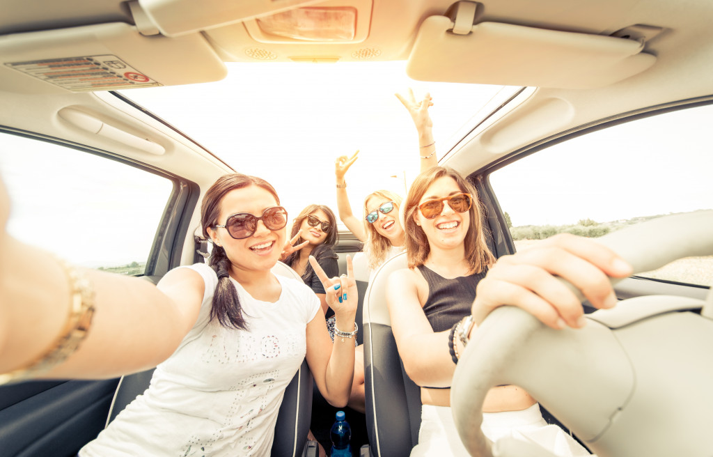 A group of girls wearing sunglasses while posing for a selfie in a moving car