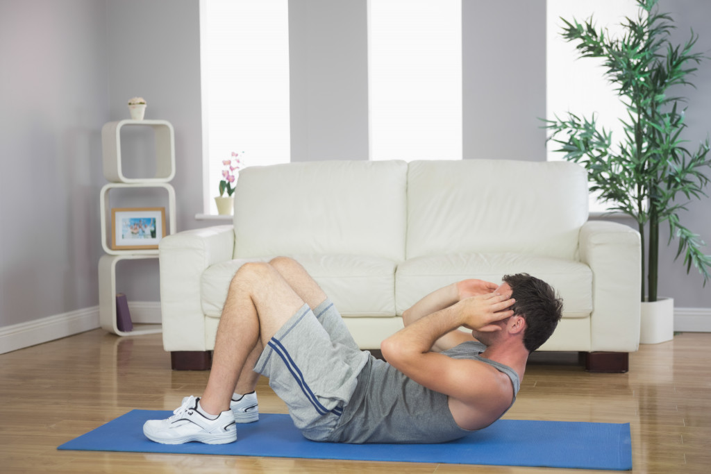 A handsome sporty man doing sit ups on a yoga mat in a home living room